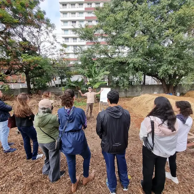 Oficina ao ar livre em um pátio de compostagem, com o facilitador explicando ao grupo diante de um quadro